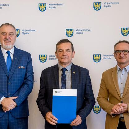 Wicemarszałek Województwa Śląskiego Grzegorz Boski, wraz z dwoma kolegami, prezentuje dokument na tle emblematu i nazwy Silesia. (wygenerowano przez AI)