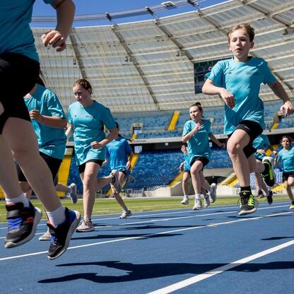 Dzieci biegają po niebieskim torze w pustym stadionie, przygotowując się do Eurowydarzenia Lekkoatletycznego. (wygenerowano przez AI)