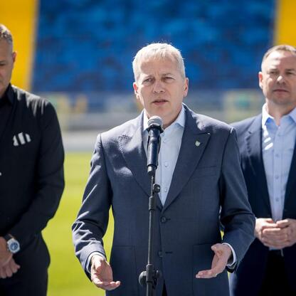 Marszałek Wojciech Saługa przemawia na stadionie, otoczony sekretarzem stanu i dyrektorem. (wygenerowano przez AI)