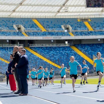 Na Superauto.pl Stadion Śląski młodzi lekkoatleci w niebieskich mundurach biegają pod okiem dorosłych na stadionie. (wygenerowano przez AI)