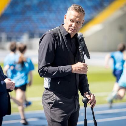 Na stadionie Superauto.pl Stadion Śląski, mężczyzna w czarnym ubraniu trzyma mikrofon i kij, podczas treningu lub imprezy sportowej. (wygenerowano przez AI)