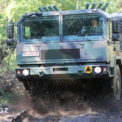 Jelcz military truck driving through muddy forest road, kicking up a cloud of mud. (wygenerowano przez AI)