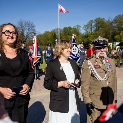 Na Śląskim Capstrzyku w Tauron Parku Śląskim, w uroczystości z okazji 105. rocznicy III Powstania Śląskiego i Dnia Flagi RP, kobieta otrzymuje nagrodę, otoczona formalnie ubranymi osobami. (wygenerowano przez AI)