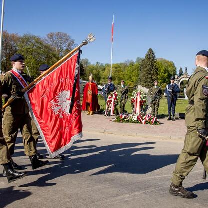 Marching soldiers carry a red flag with white emblems at Tauron Park Śląskim to commemorate the 105th anniversary of the Third Silesian Uprising and the Day of the Polish Flag. (wygenerowano przez AI)