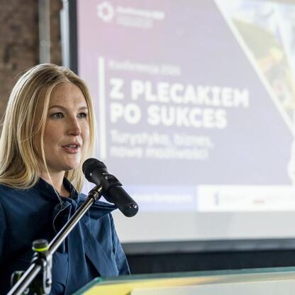 Joanna Bojczuk, członek Zarządu Województwa Śląskiego, przemawia na podium podczas konferencji w Muzeum Hutnictwa Cynku Walcownia w Katowicach. (wygenerowano przez AI)