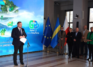 Podczas konferencji dotyczącej poprawy jakości powietrza województwa śląskiego, dwie osoby stoją na podium, jedna przemawia do mikrofonu, druga trzyma dokument. (wygenerowano przez AI)