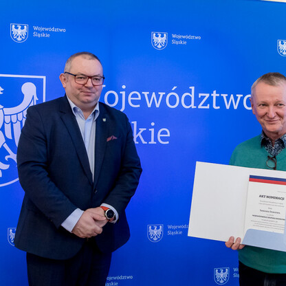 Dwóch pracowników Silesia stanęło przed sztandarem województwa, jednego z nich w ciemnym garniturze i okularach, drugiego w zielonej bluzie, trzymając dokument i certyfikat. (wygenerowano przez AI)