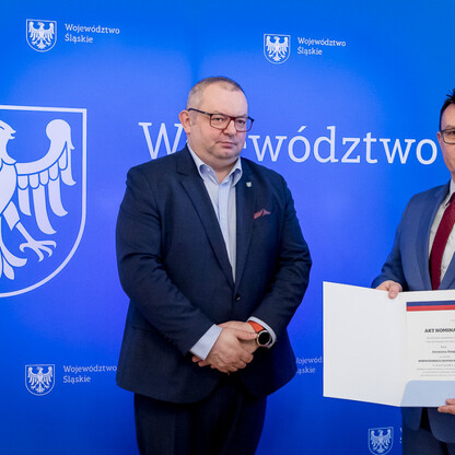 Dwóch mężczyzn w strojach formalnych przedstawiających Województwo Śląskie, jednym z nich trzymając dokument 