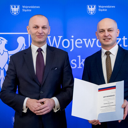 Dwóch mężczyzn w strojach formalnych przedstawiających Województwo Śląskie, jednym z nich wręczony dokument 