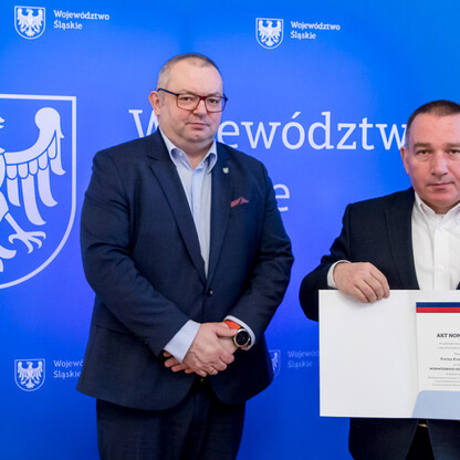 Dwóch mężczyzn w niebieskim tle Śląska, jednego z nich w ręku trzyma dokument 