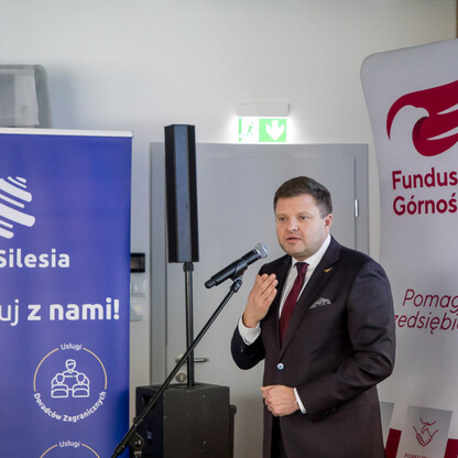Mężczyzna w garniturze przemawia na podium podczas konferencji promującej Fundusz Górnośląski SA i inicjatywy 