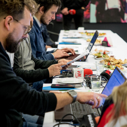 Grupa ludzi siedzących wokół długiego stołu, uczestniczących w spotkaniu lub warsztacie, z laptopami i dokumentami. (wygenerowano przez AI)