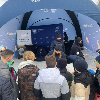 Grupa osób zgromadzona pod namiotem Śląskiego Parku Nauki, gdzie odbywa się edukacyjna impreza dla rodzin. (wygenerowano przez AI)