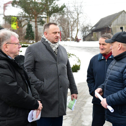 Grupa czterech mężczyzn w zimowym stroju rozmawiających na zewnątrz w zimowej scenerii, przedstawiającej zakończenie modernizacji drogi wojewódzkiej od Czernichowa do skrzyżowania z DW 946 w Żywcu-Ocz (wygenerowano przez AI)
