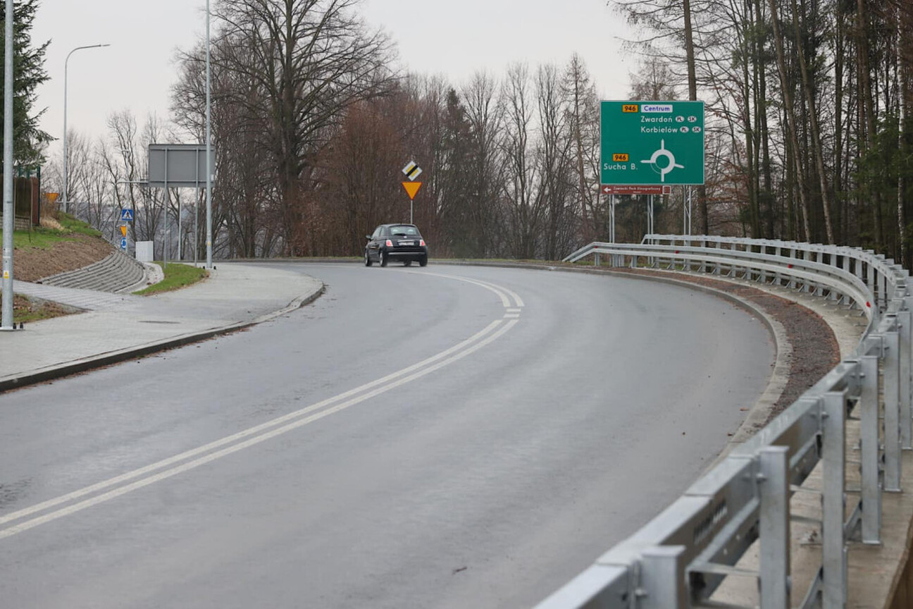 Czterech ludzi w deszczu z parasolkami, ubrani w zimowe ubrania, dyskutują o modernizacji drogi wojewódzkiej w Beskidzie Żywieckim. (wygenerowano przez AI)