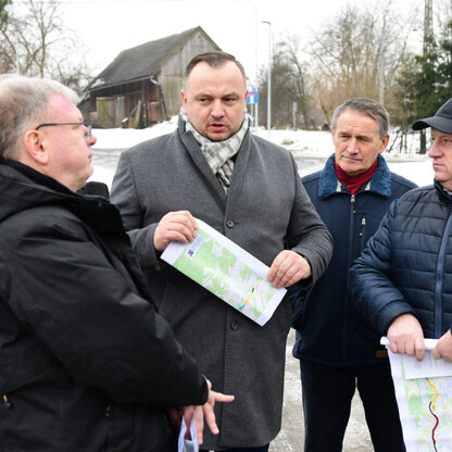 Grupa czterech mężczyzn dyskutuje o modernizacji drogi wojewódzkiej w okolicach Czernichowa, podczas wizyty w regionie. (wygenerowano przez AI)