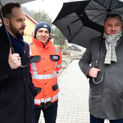 Trzech mężczyzn w mundurach i odblaskowym kurtce, trzymający parasole, stoją na drodze podczas deszczu, podczas inspekcji drogi Wojewódzkiej 948. (wygenerowano przez AI)