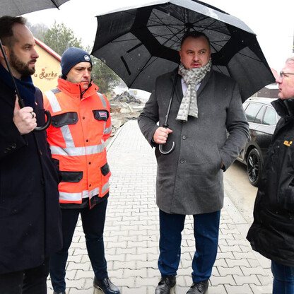 Czterech ludzi w deszczu z parasolkami, ubrani w zimowe ubrania, dyskutują o modernizacji drogi wojewódzkiej w Beskidzie Żywieckim. (wygenerowano przez AI)