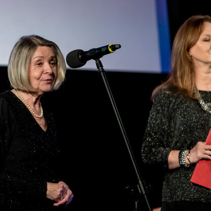 Na zdjęciu z nagrodzonej uroczystości Marszałka Województwa Śląskiego Culture Awards, dwie kobiety na scenie: jedna mówiąca, druga trzymająca czerwoną kopertę. (wygenerowano przez AI)