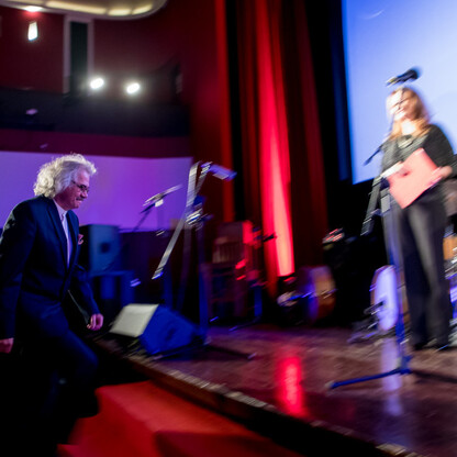 Na scenie podczas uroczystości wręczenia nagród Marszałka Województwa Śląskiego Culture Awards, mężczyzna gra na klawiaturze, podczas gdy dwie osoby w garniturach trzymają certyfikaty. (wygenerowano przez AI)