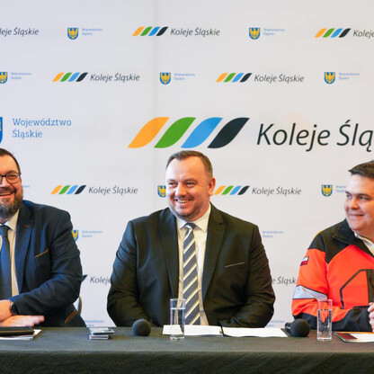 Grupa osób w garniturach i kamizelce odblaskowej siedzi przy stole, uczestnicząc w spotkaniu Kolei Śląskich. (wygenerowano przez AI)