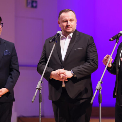 Trzech mężczyzn na scenie z mikrofonami, prawdopodobnie podczas konferencji prasowej projektu 