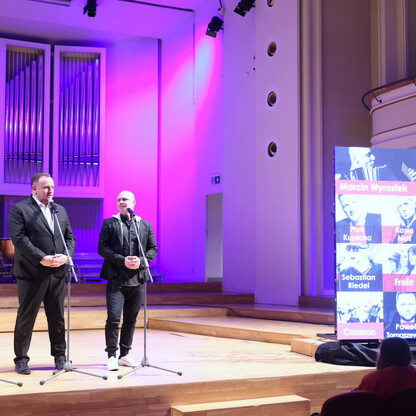 Trzech mężczyzn na scenie z mikrofonami, przedstawiająca koncert 