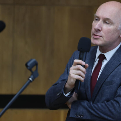 Mężczyzna w garniturze przemawia do mikrofonu, otaczony w konferencji w Sosnowcu. (wygenerowano przez AI)