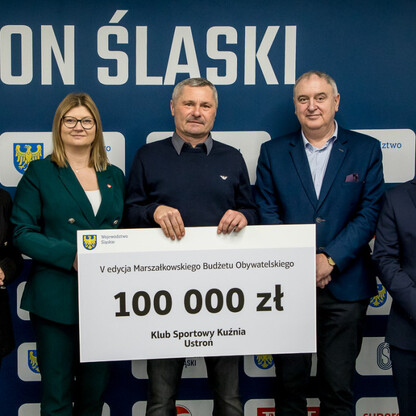 Grzegorz Boski, wicemarszałek województwa, prezentuje symboliczny czek na 100,000 zł na Stadionie Śląskim. (wygenerowano przez AI)