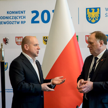 Dwa mężczyźni w strojach formalnych dyskutują na konwencie prezydentów sejmików województw RP 2017, dotyczącym problemu nielegalnego składowania odpadów. (wygenerowano przez AI)