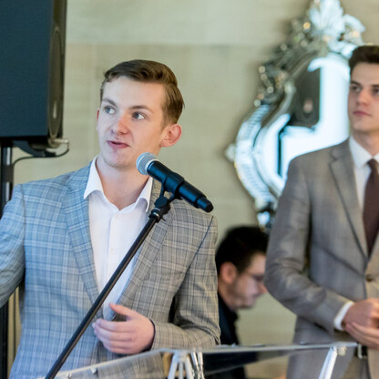 Mężczyzna w kraciastej kamizelce przemawia do mikrofonu na konwencie wojewódzkich przewodniczących sejmików, omawiając problem nielegalnego składowania odpadów. (wygenerowano przez AI)