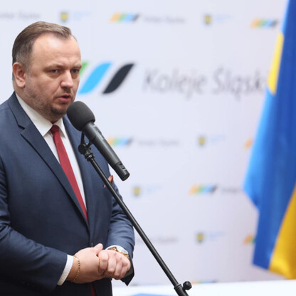 Mężczyzna w garniturze przemawia na podium z mikrofonem, przedstawiając nowe elektryczne zespoły Kolei Śląskich. (wygenerowano przez AI)