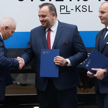 Trzy mężczyźni w garniturach stoją przed pociągiem z napisem 