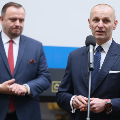 Dwa mężczyźni w strojach formalnych, przedstawiają logo Kolei Śląskich, jednego mówiące, drugi gestykulujący. (wygenerowano przez AI)