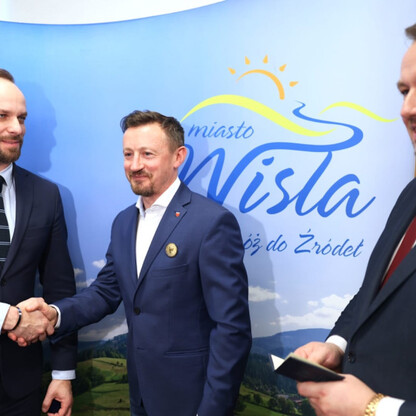 Trzech mężczyzn w strojach formalnych trzyma się za ręce przed logo i nazwą Wisły, podczas uroczystości wręczenia Medalu im. Bogumiła Hoffa. (wygenerowano przez AI)