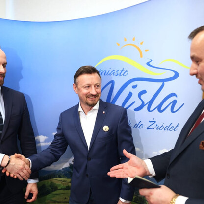 Trzech mężczyzn w strojach formalnych trzyma się za ręce przed logo i nazwą Wisły, podczas uroczystości wręczenia Medalu im. Bogumiła Hoffa. (wygenerowano przez AI)