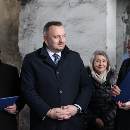 Zdjęcie przedstawia grupę ludzi w formalnym uroczystości, związanej z adaptacją Szybu Staszic w Tarnowskich Górach, wpisanego na listę światowego dziedzictwa UNESCO. (wygenerowano przez AI)