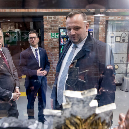 Trzech mężczyzn w garniturach stoi przed szklaną wystawą w muzeum, podpisując umowę o współprowadzeniu Kopalni Ignacy w Rybniku. (wygenerowano przez AI)