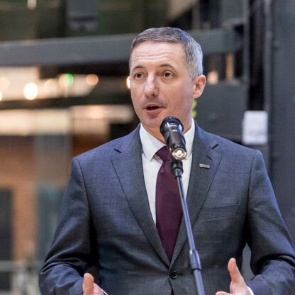 Mężczyzna w ciemnym garniturze i krawacie przemawia do mikrofonu, prawdopodobnie na konferencji prasowej w Śląsku. (wygenerowano przez AI)