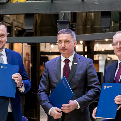 Trzech mężczyzn w formalnym stroju trzymają niebieskie foldery, przedstawiają umowę o współprowadzeniu Zabytkowej Kopalni Ignacy w Rybniku. (wygenerowano przez AI)