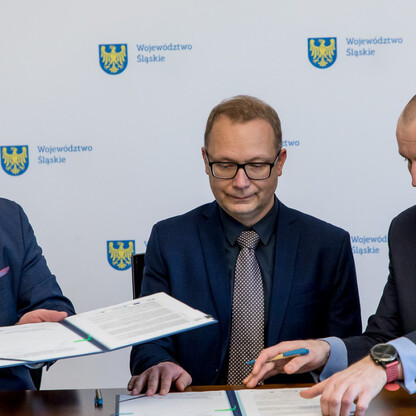Trzech mężczyzn w strojach formalnych podpisuje dokument, reprezentując Województwo Śląskie w procesie adaptacji do zmian klimatu. (wygenerowano przez AI)