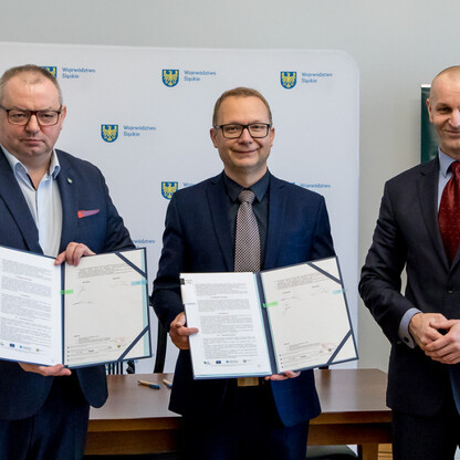 Trzech mężczyzn w strojach urzędniczych trzymają dokumenty, przedstawiając Regionalny Plan Adaptacji do Zmian Klimatu dla Województwa Śląskiego. (wygenerowano przez AI)