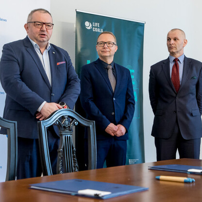 Trzech mężczyzn w strojach formalnych przed banerem 