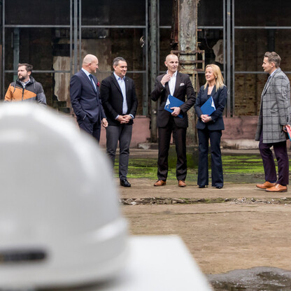 Grupa ludzi w biznesowych strojach inspektuje przestrzeń przemysłową, przygotowując ją do przyszłego centrum miasta w Dąbrowie Górniczej. (wygenerowano przez AI)