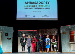 Mężczyzna w niebieskim dresie trzyma tradycyjny polski kufel, uczestnicząc w uroczystości związanych z programem Ambasadorzy Srebrnego Pokolenia. (wygenerowano przez AI)