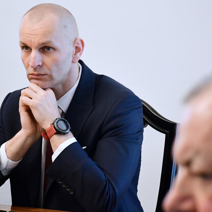 Mężczyzna w ciemnym garniturze i białej koszuli siedzi przy stole, wydając się w myślach lub słuchając uważnie. (wygenerowano przez AI)