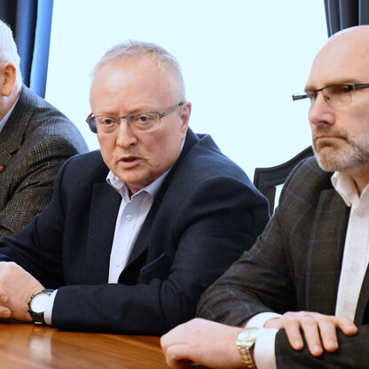 Trzech mężczyzn w garniturach siedzi przy stole, dyskutując o potencjalnym wznowieniu kursów kolejowych Gliwice-Rybnik. (wygenerowano przez AI)