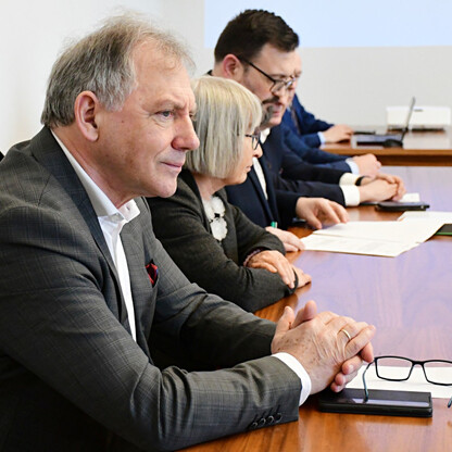 Grupa ludzi w formalnym ubiorze siedzi przy długim drewnianym stole w Gliwickim Sejmiku Śląskim, omawiając potencjalne reaktywowanie połączenia kolejowego Gliwice-Rybnik. (wygenerowano przez AI)