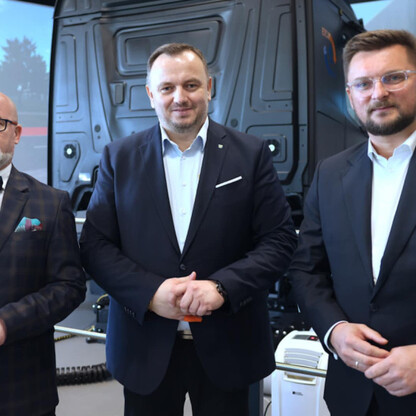 Trzech mężczyzn w ciemnych garniturach stojących przed ekranem z wizualizacją ciężarówki, związani z otwarciem Centrum Bezpieczeństwa Ruchu Drogowego w Katowicach. (wygenerowano przez AI)