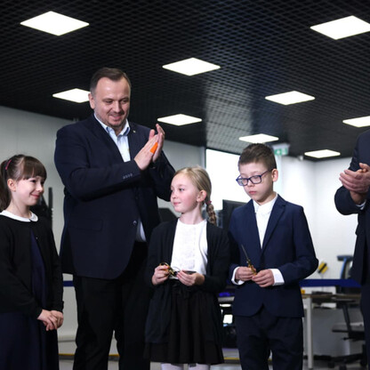 Grupa dorosłych i dzieci w modernistycznym pomieszczeniu, uczestniczących w uroczystości promującej bezpieczeństwo ruchu drogowego. (wygenerowano przez AI)